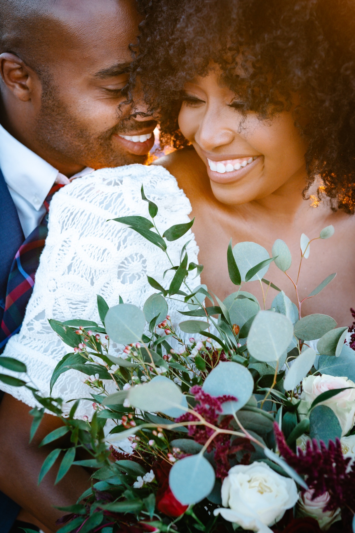 Bride and groom smiling close together behind a lush bouquet