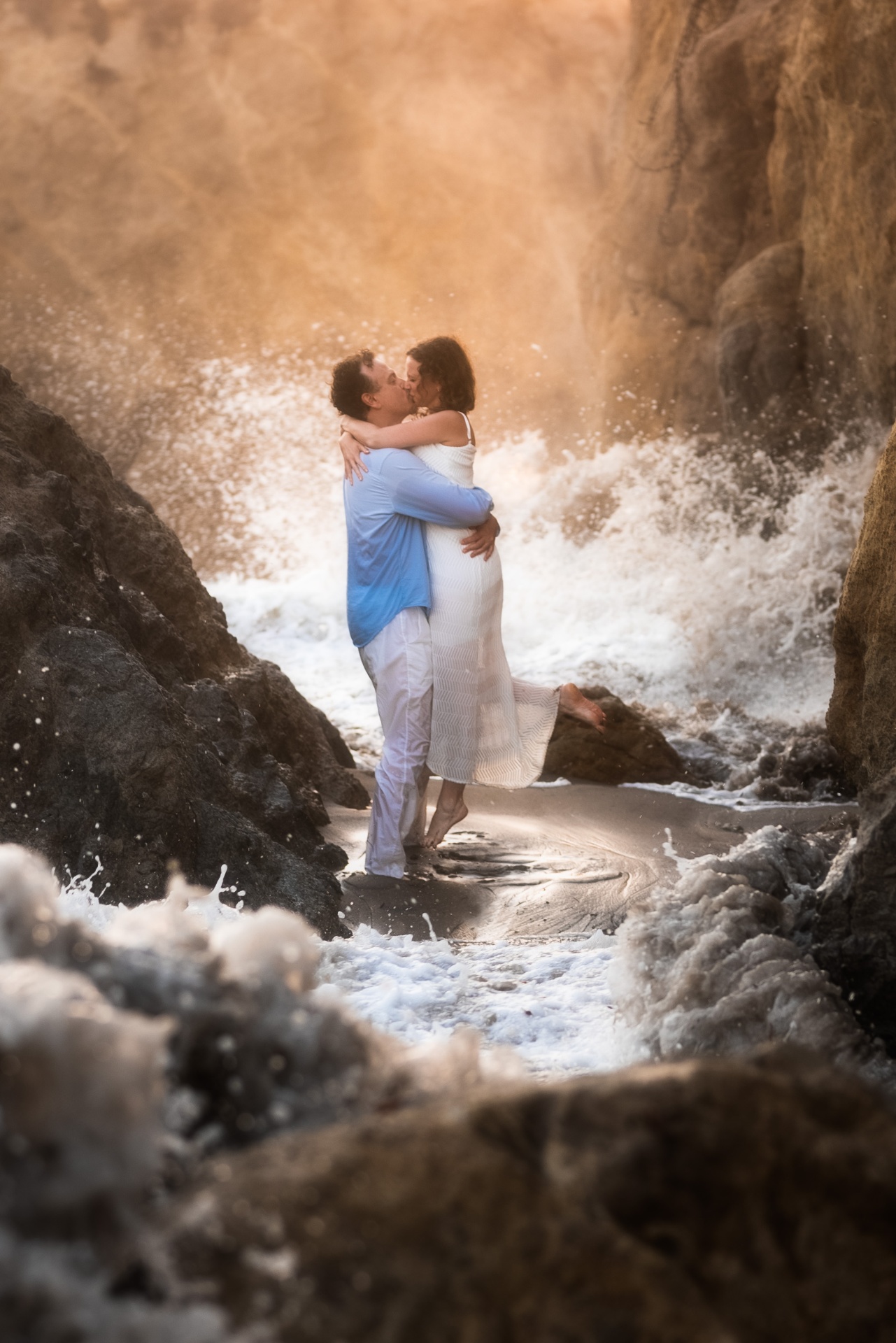 Couple sharing a kiss between coastal rocks at golden hour